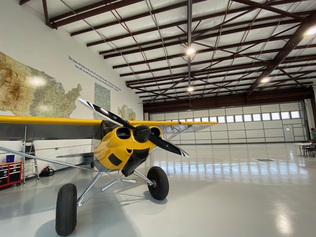 white matte epoxy flooring installed in an airplane hanger. yellow airplane parked in hanger