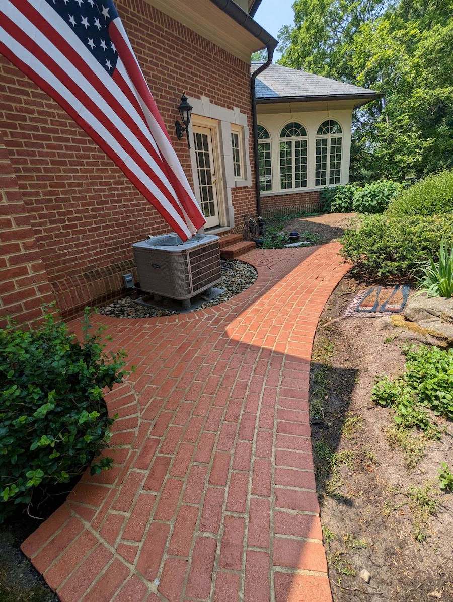 a freshly pressure washed brick walkway leading to a house with an american flag