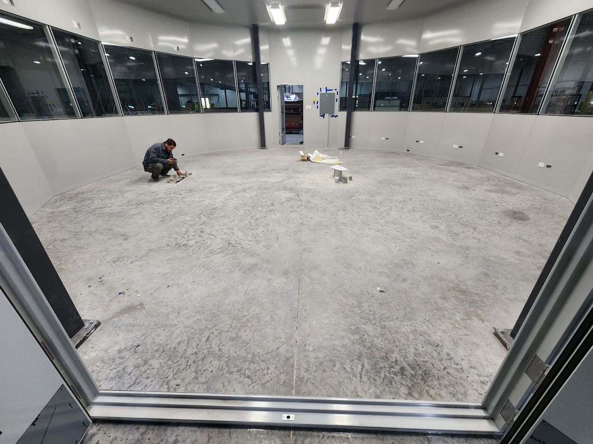 a man sits on a concrete floor in a room with a lot of windows