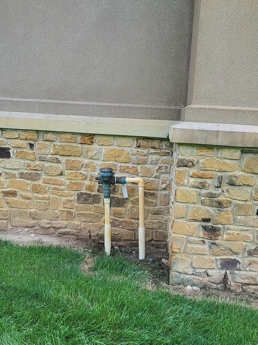 a brick wall with a hose attached to it that has irrigation stains