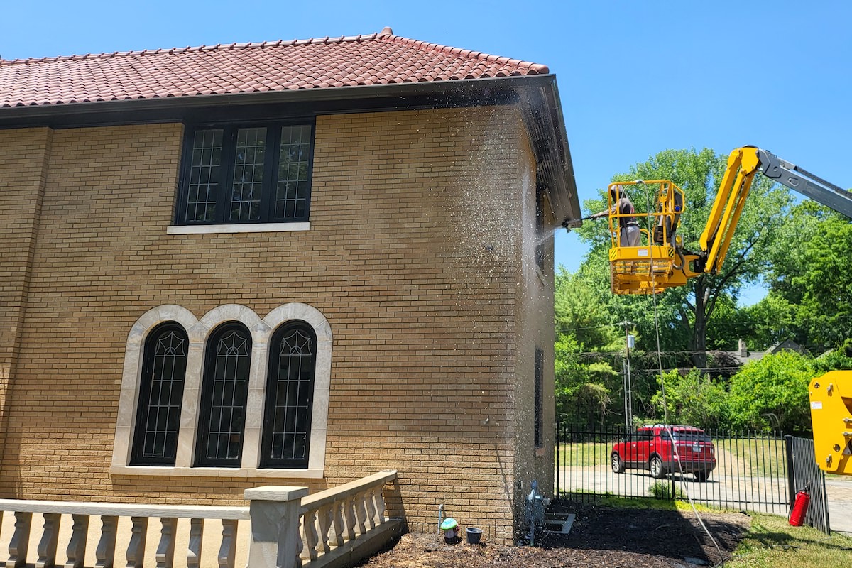 a yellow crane with a man pressure washing a brick building