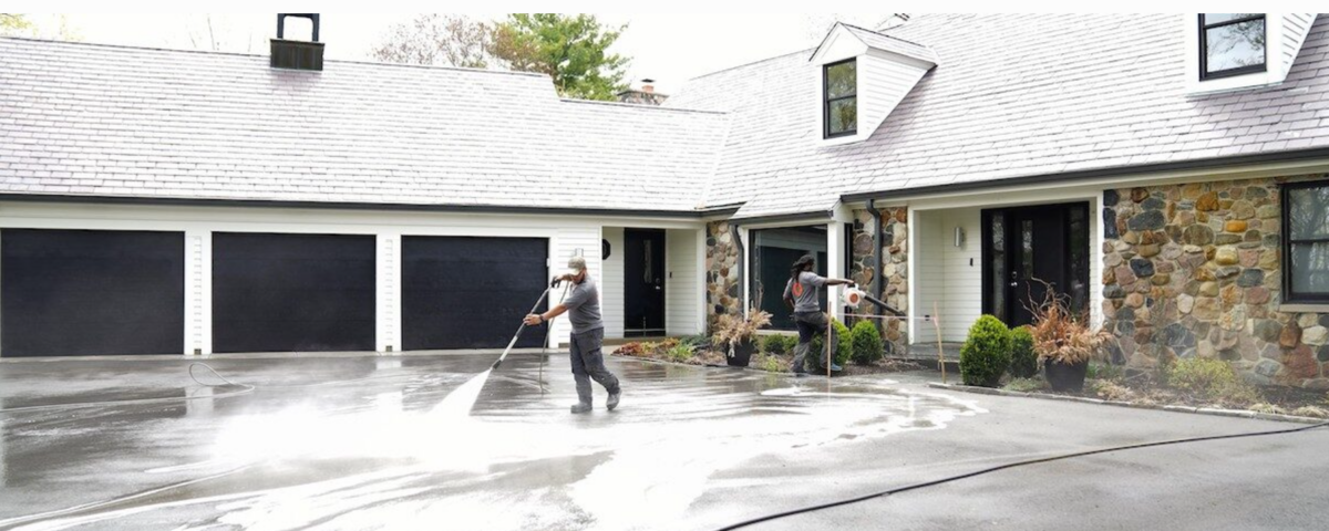 two men are cleaning a driveway in front of a house