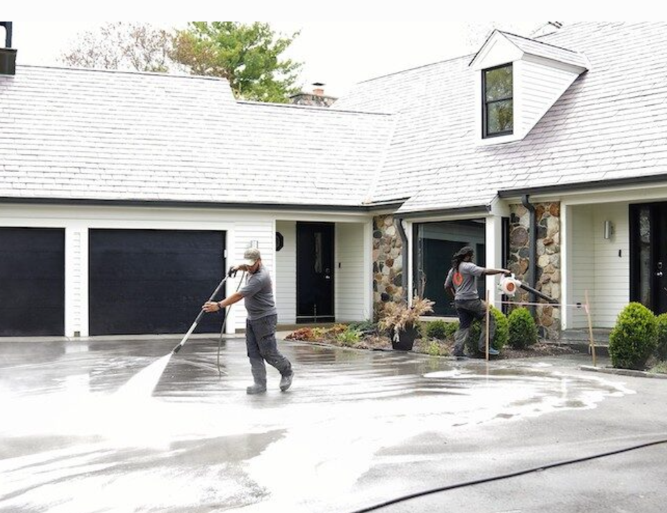 two men are cleaning a driveway in front of a house